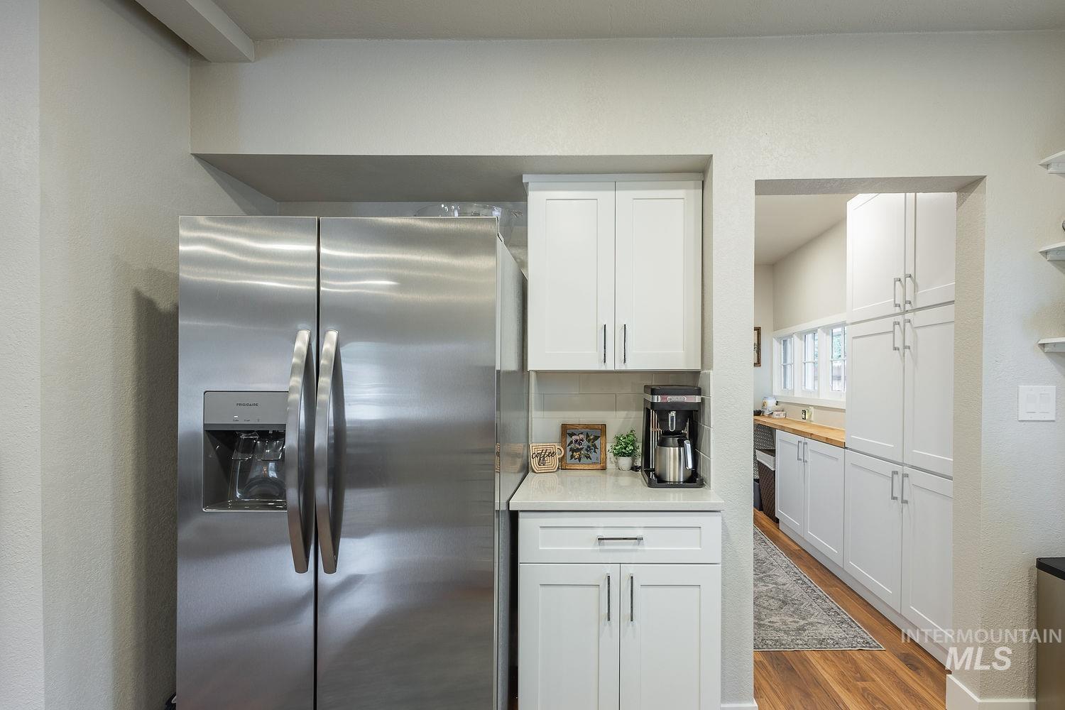 Kitchen featuring stainless steel fridge, white cabinetry, dark wood-type flooring, open shelves, and light stone countertops