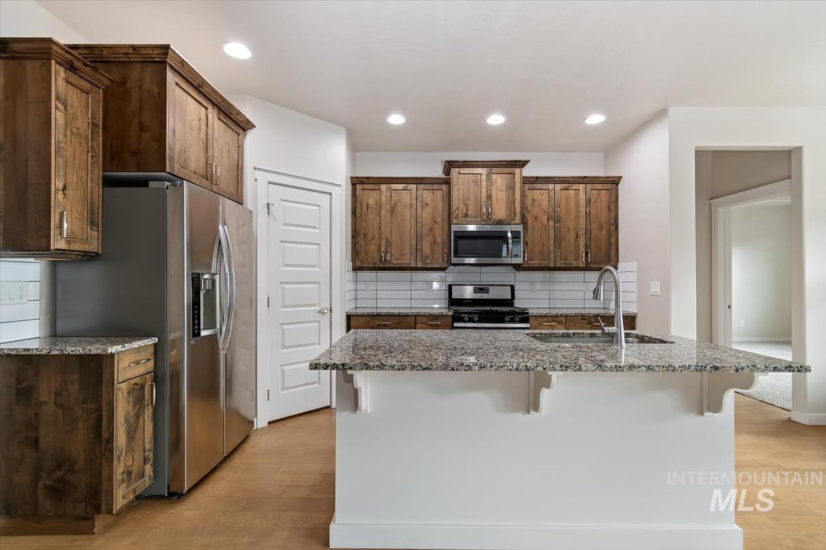Kitchen featuring backsplash, light stone counters, a breakfast bar, light wood finished floors, and recessed lighting