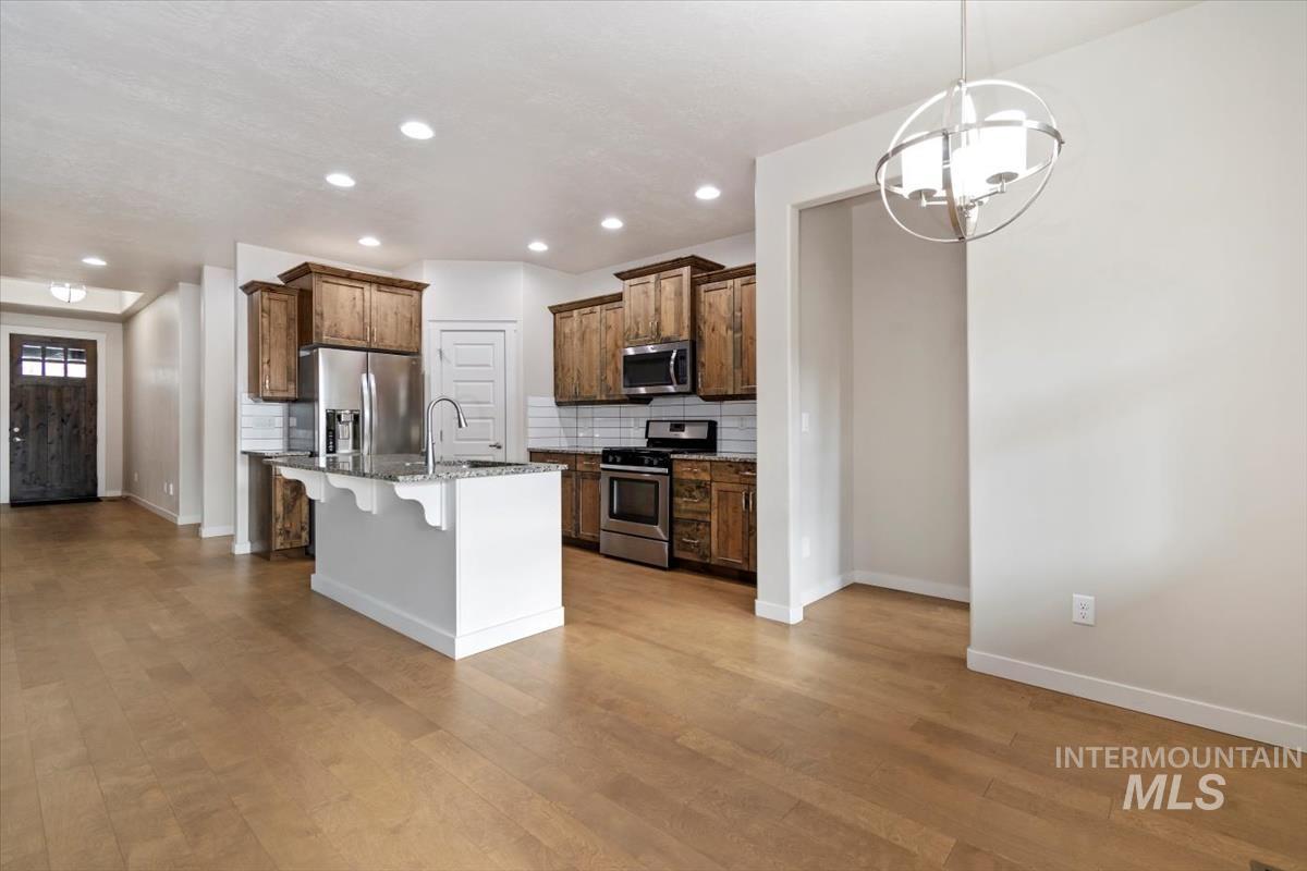 Kitchen with a breakfast bar, decorative backsplash, appliances with stainless steel finishes, hanging light fixtures, and recessed lighting