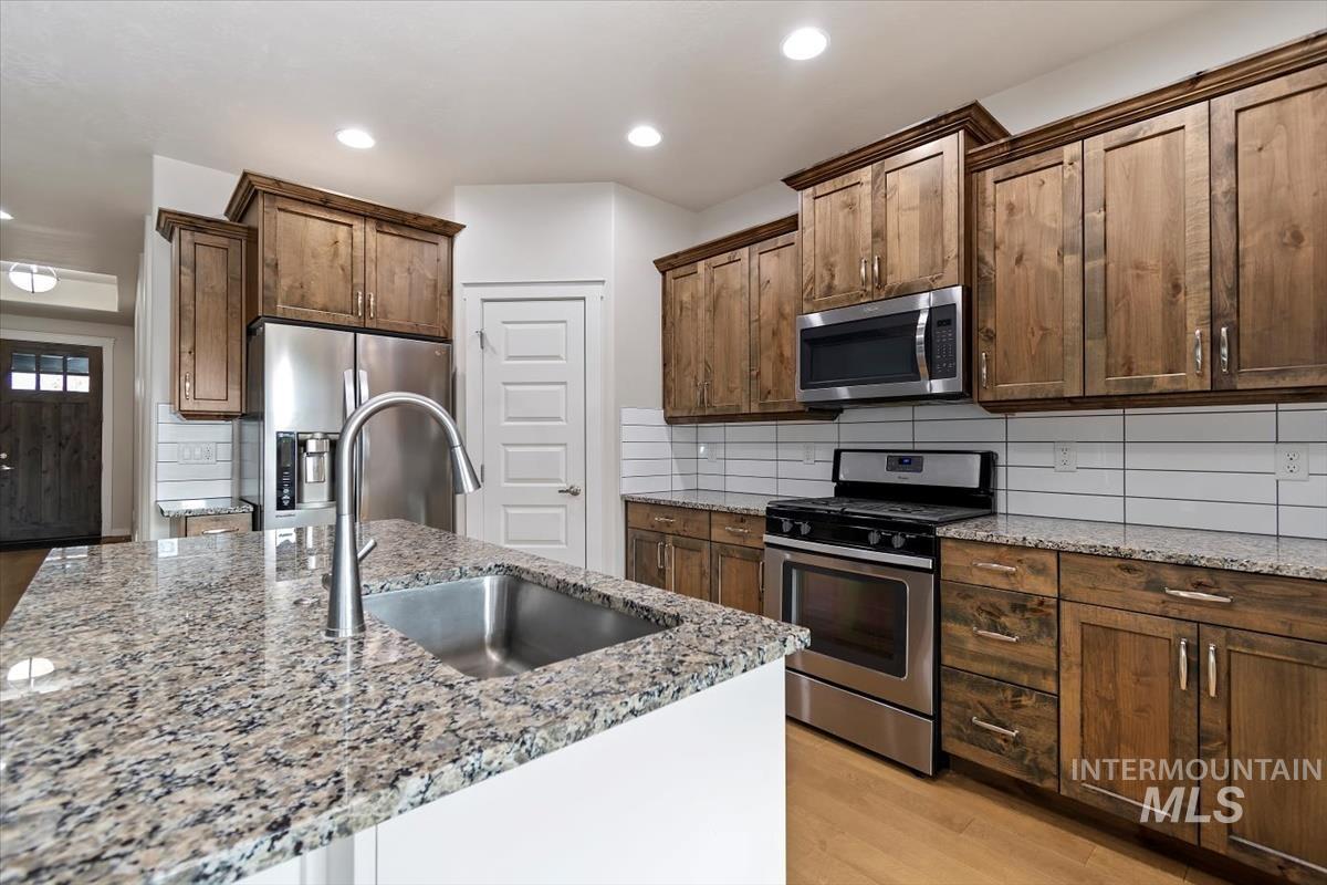 Kitchen featuring stainless steel appliances, tasteful backsplash, light stone counters, light wood-style flooring, and recessed lighting