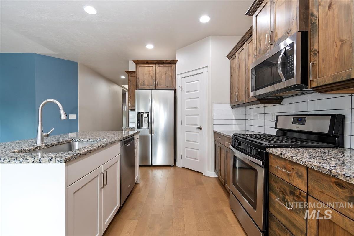 Kitchen with appliances with stainless steel finishes, light wood-style floors, light stone counters, recessed lighting, and tasteful backsplash