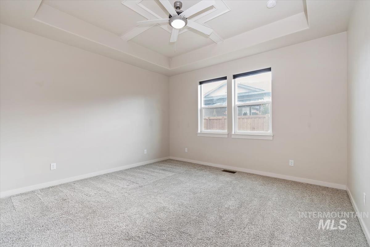 Carpeted empty room with a tray ceiling and ceiling fan