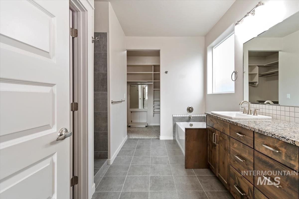 Full bath with a spacious closet, vanity, a garden tub, and dark tile patterned flooring