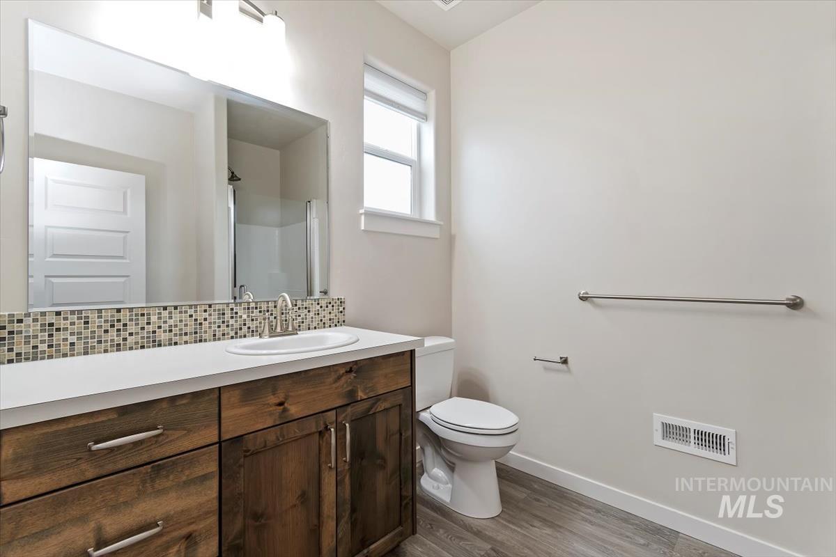 Full bath featuring dark wood finished floors, vanity, a shower, and decorative backsplash