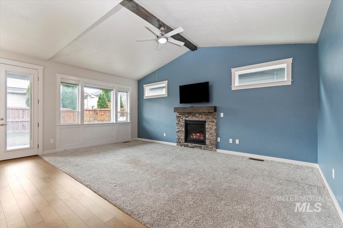 Unfurnished living room with a stone fireplace, a ceiling fan, wood finished floors, and carpet floors