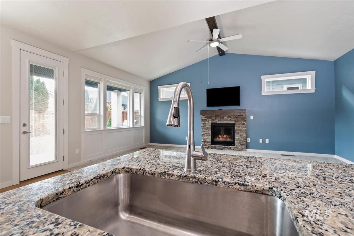 Kitchen featuring light stone counters, a stone fireplace, a ceiling fan, and open floor plan