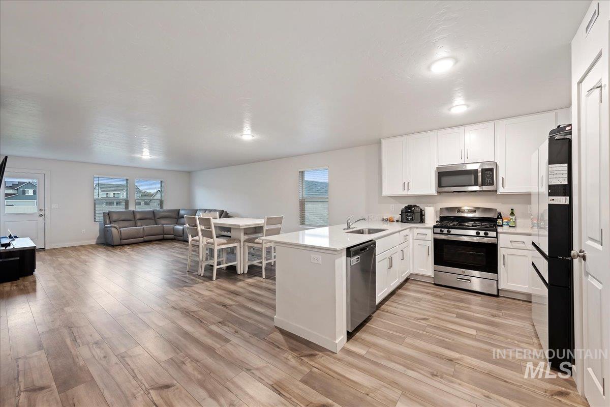 Kitchen with a peninsula, open floor plan, appliances with stainless steel finishes, white cabinets, and light wood finished floors