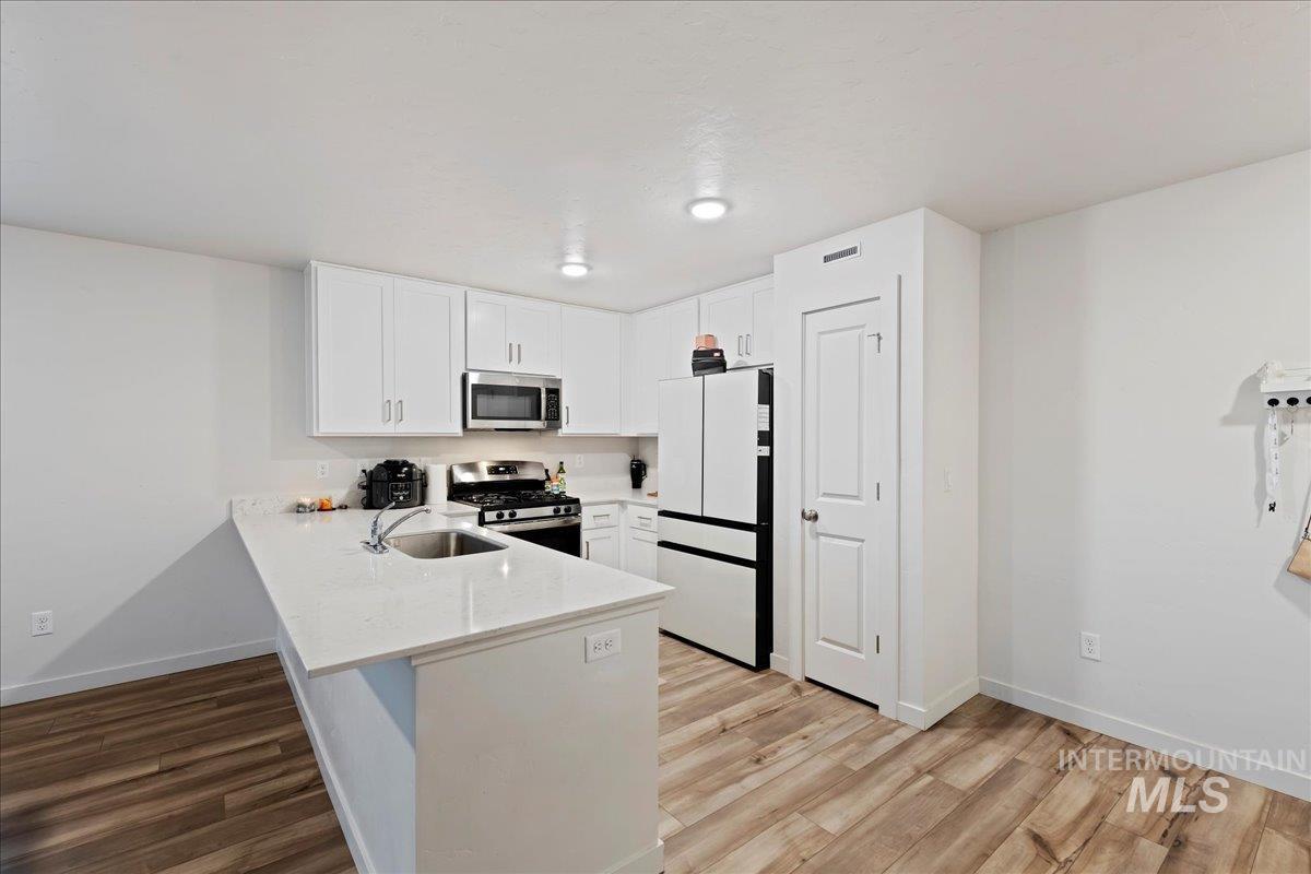 Kitchen with a peninsula, white cabinets, appliances with stainless steel finishes, light stone countertops, and light wood-style floors