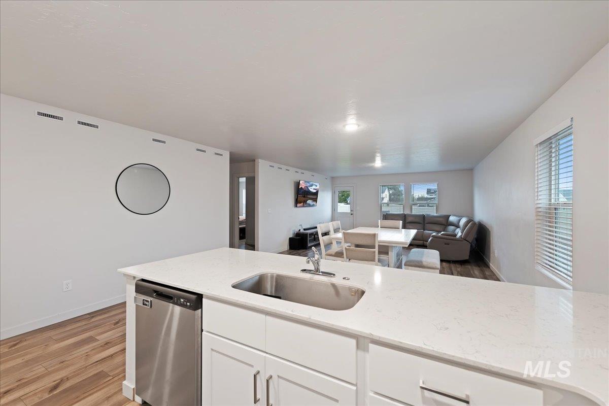 Kitchen featuring white cabinets, light wood finished floors, open floor plan, dishwasher, and light stone counters