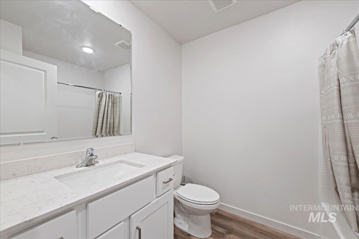 Bathroom with dark wood-style floors, vanity, and shower / bath combination with curtain