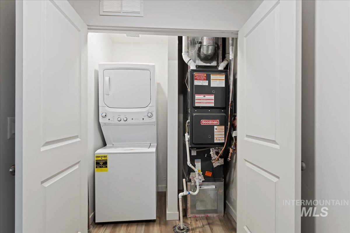 Laundry area with stacked washer and clothes dryer, light wood-type flooring, and heating unit