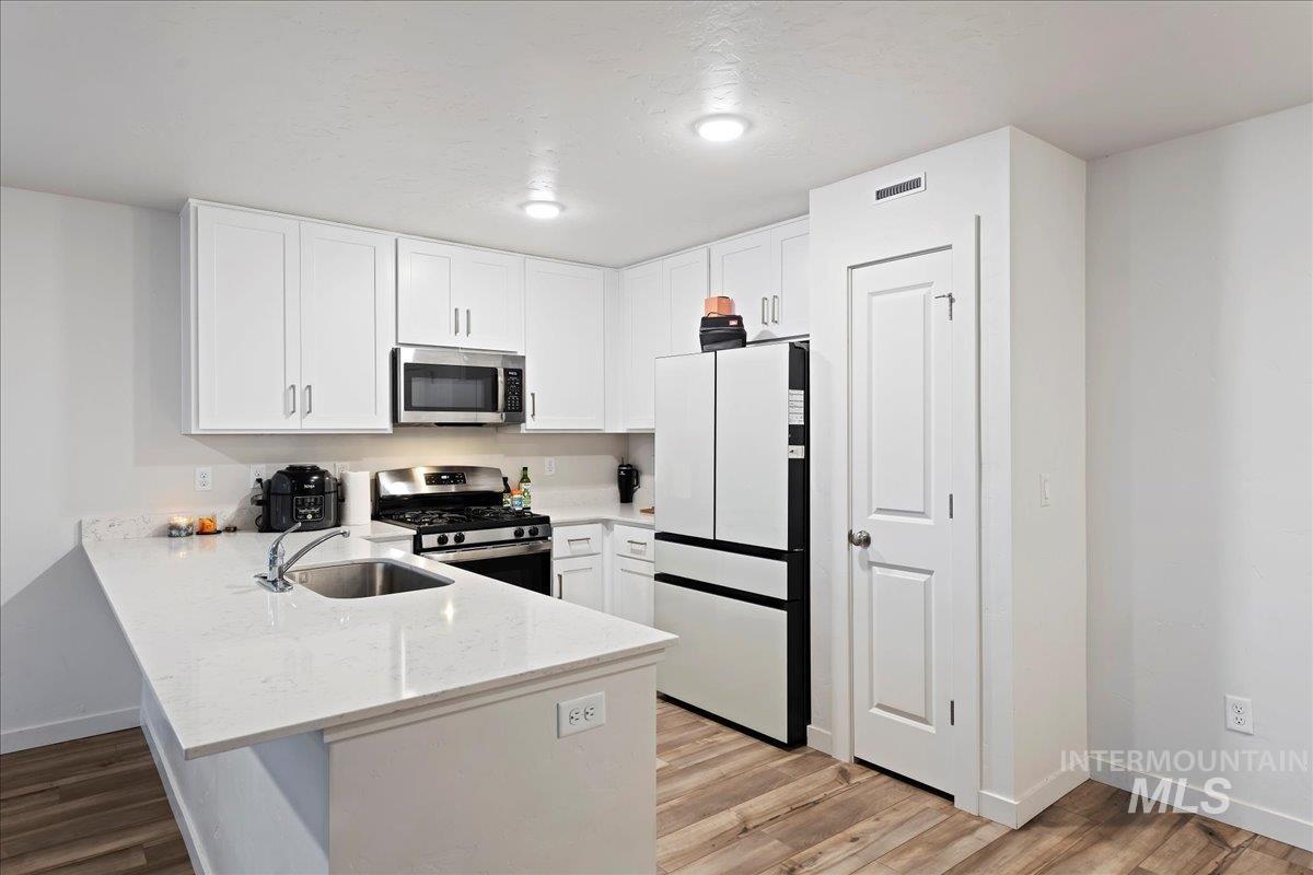 Kitchen featuring stainless steel appliances, light stone countertops, white cabinets, a peninsula, and light wood-style floors