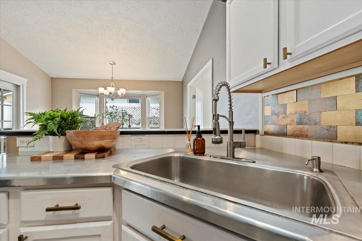 Kitchen with white cabinetry, decorative backsplash, a textured ceiling, stainless steel counters, and decorative light fixtures