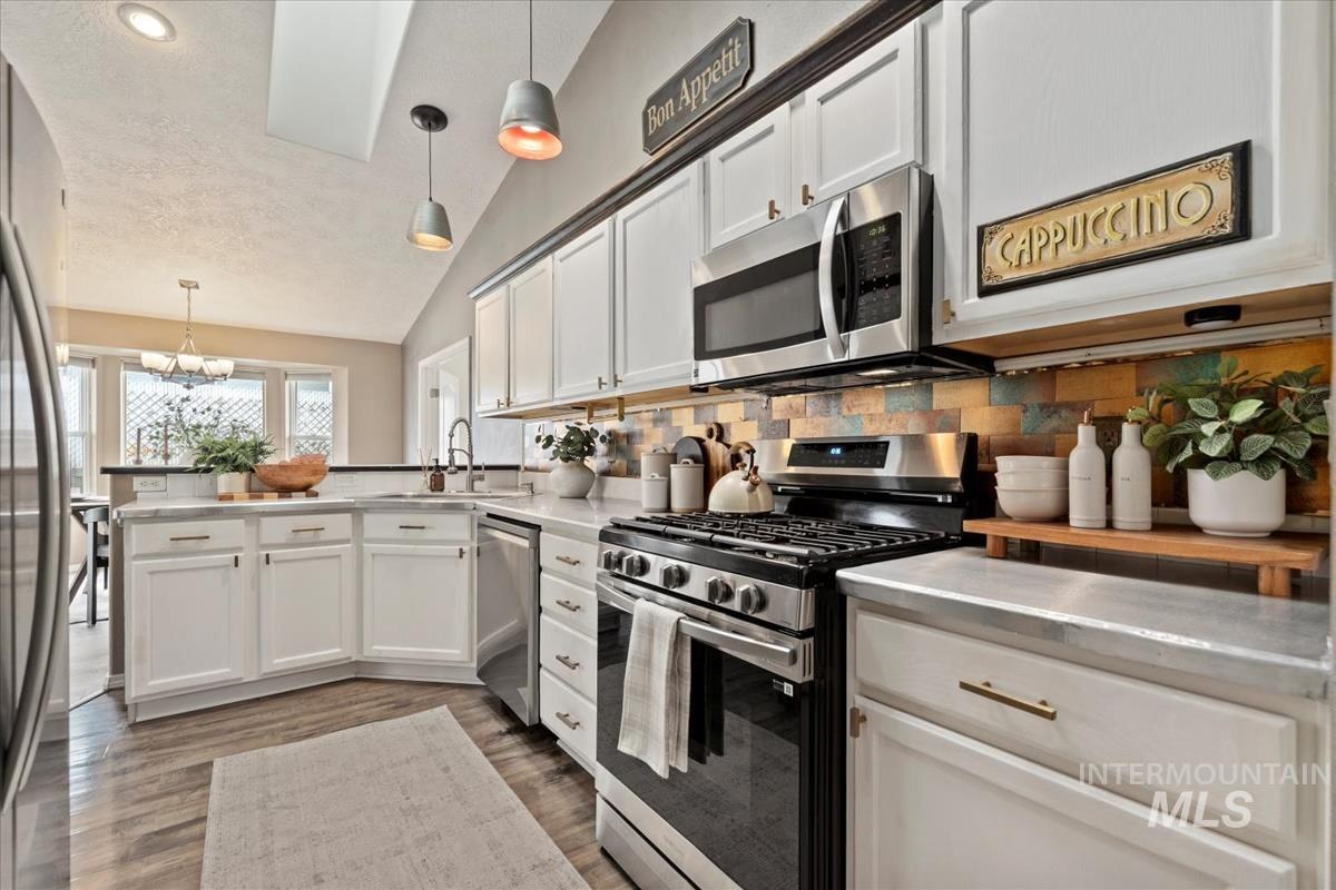 Kitchen featuring stainless steel appliances, decorative backsplash, pendant lighting, white cabinets, and a peninsula