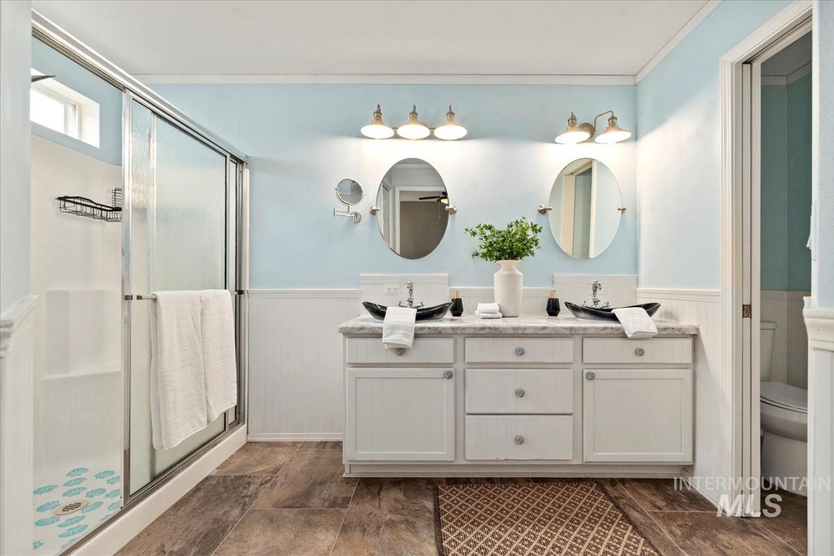Bathroom with a stall shower, double vanity, a wainscoted wall, and ornamental molding
