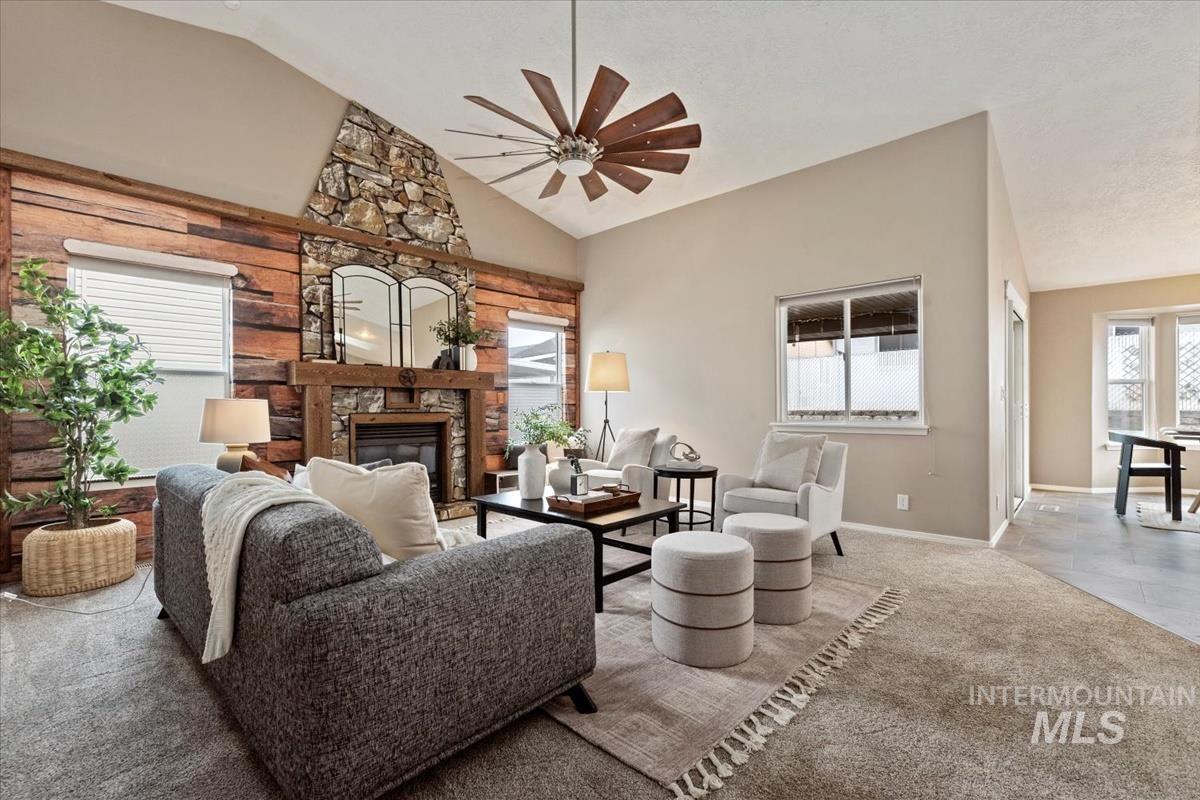 Carpeted living area with a stone fireplace, a ceiling fan, high vaulted ceiling, and tile patterned floors