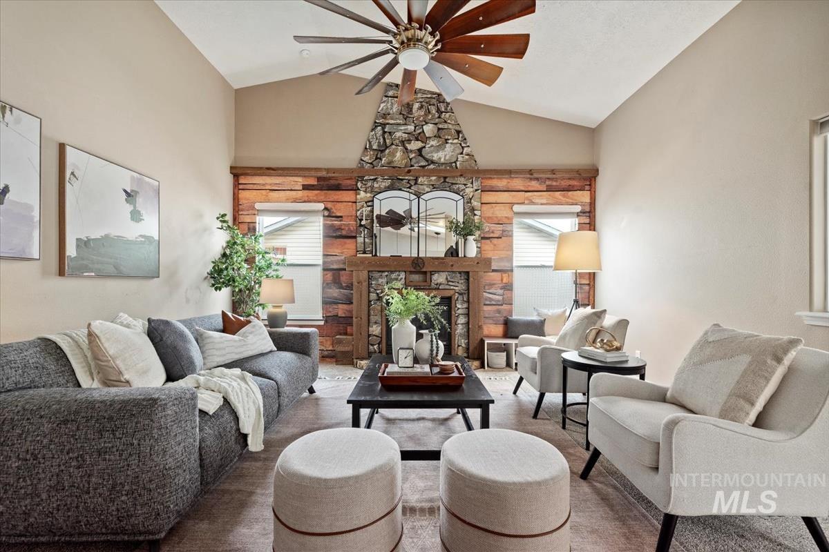 Living area with healthy amount of natural light, a stone fireplace, ceiling fan, and high vaulted ceiling