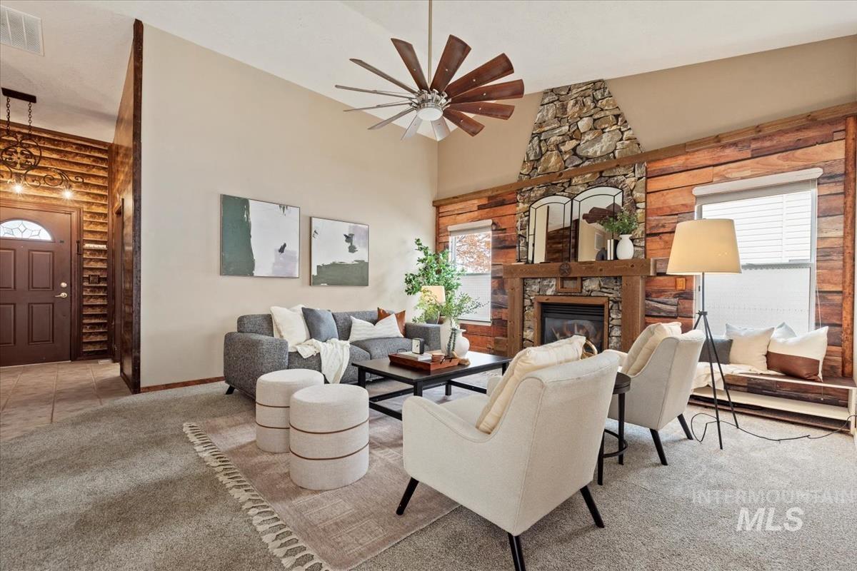 Living room with log walls, light carpet, a stone fireplace, and a towering ceiling
