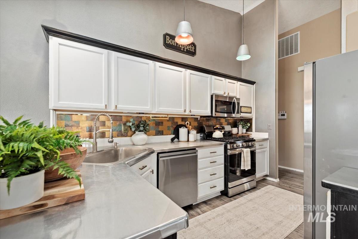 Kitchen featuring backsplash, stainless steel appliances, pendant lighting, a high ceiling, and light wood-type flooring