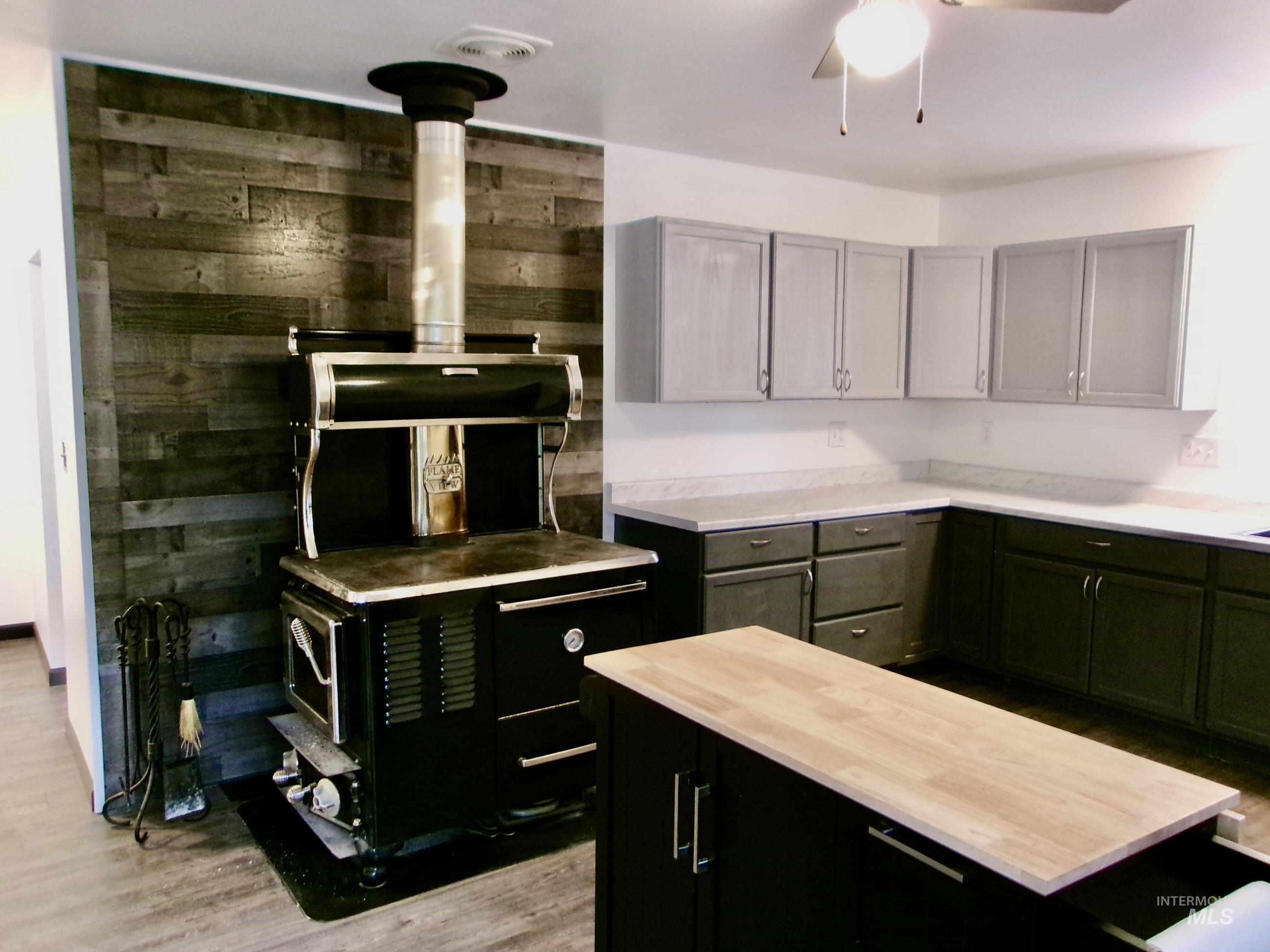 Kitchen featuring light wood-style floors, wooden walls, a wood stove, dark cabinets, and ceiling fan
