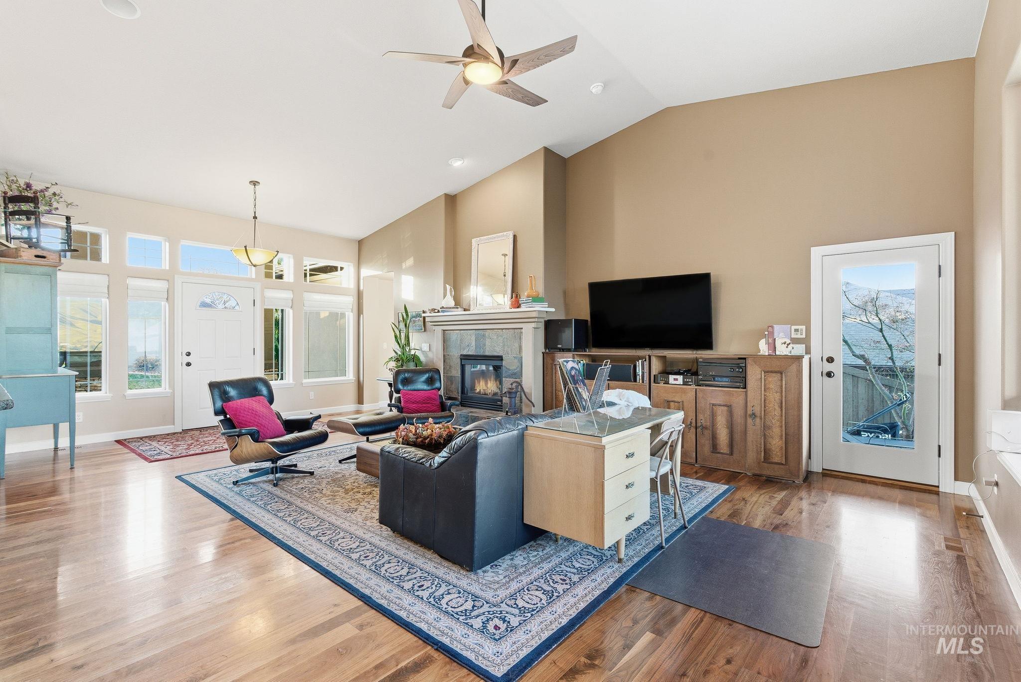 Living area featuring a fireplace, high vaulted ceiling, healthy amount of natural light, light wood finished floors, and a ceiling fan