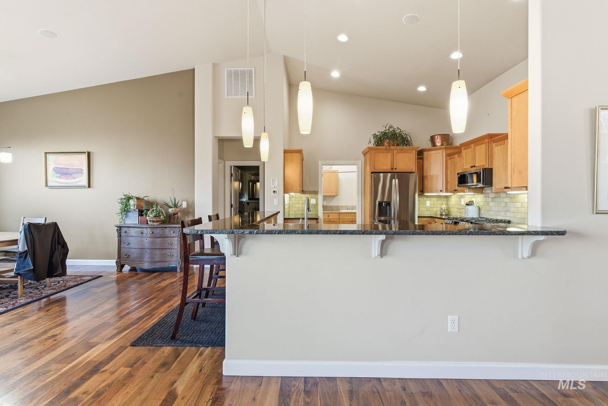Kitchen featuring a kitchen breakfast bar, pendant lighting, dark stone countertops, backsplash, and high vaulted ceiling
