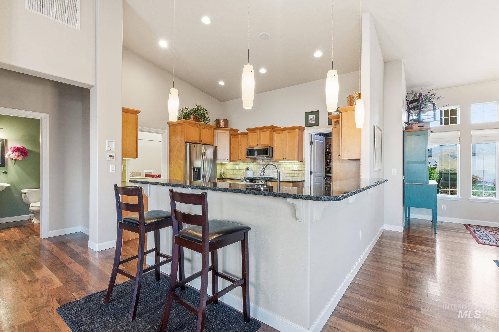 Kitchen featuring a breakfast bar, tasteful backsplash, decorative light fixtures, appliances with stainless steel finishes, and high vaulted ceiling