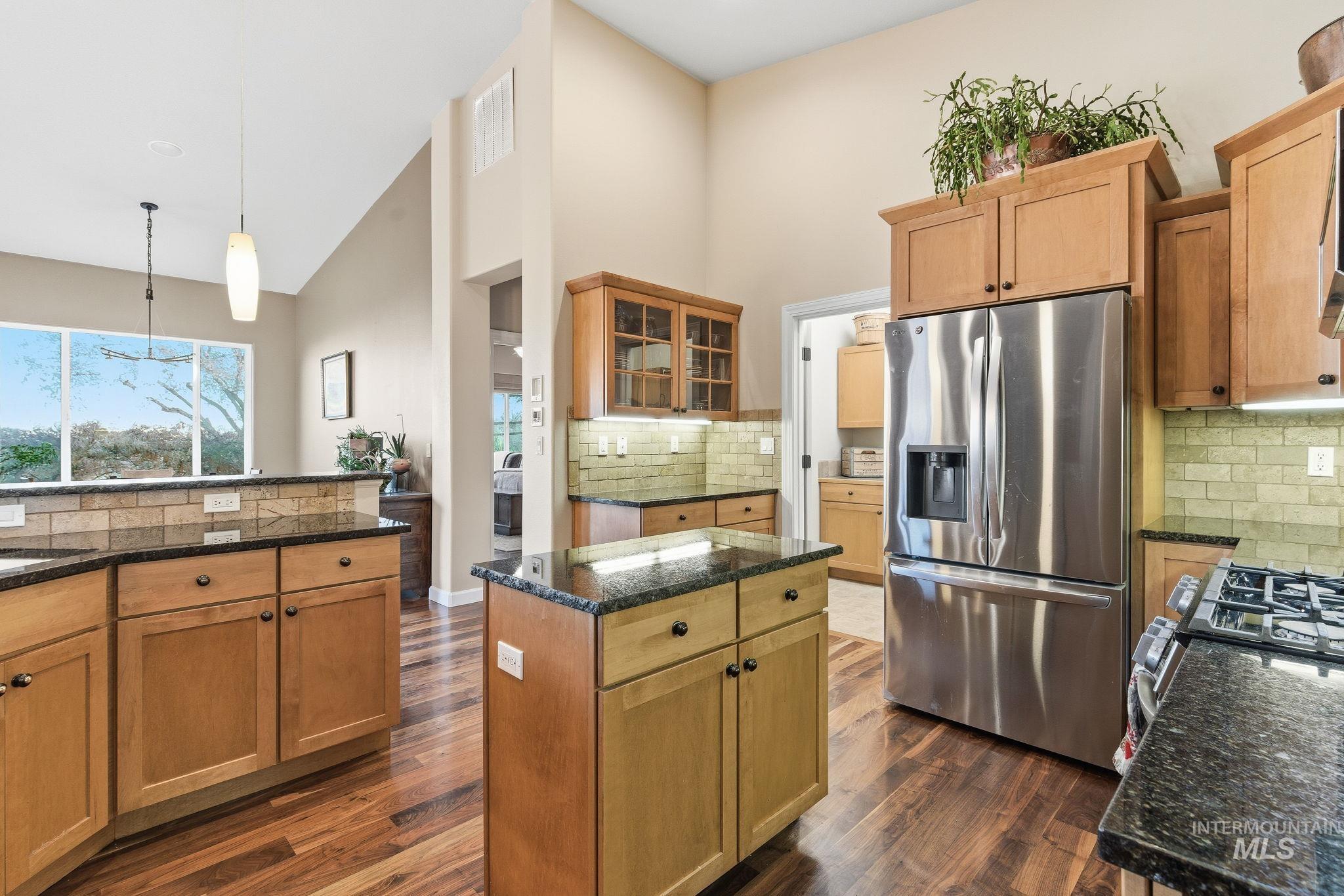 Kitchen with tasteful backsplash, appliances with stainless steel finishes, high vaulted ceiling, dark stone countertops, and glass insert cabinets