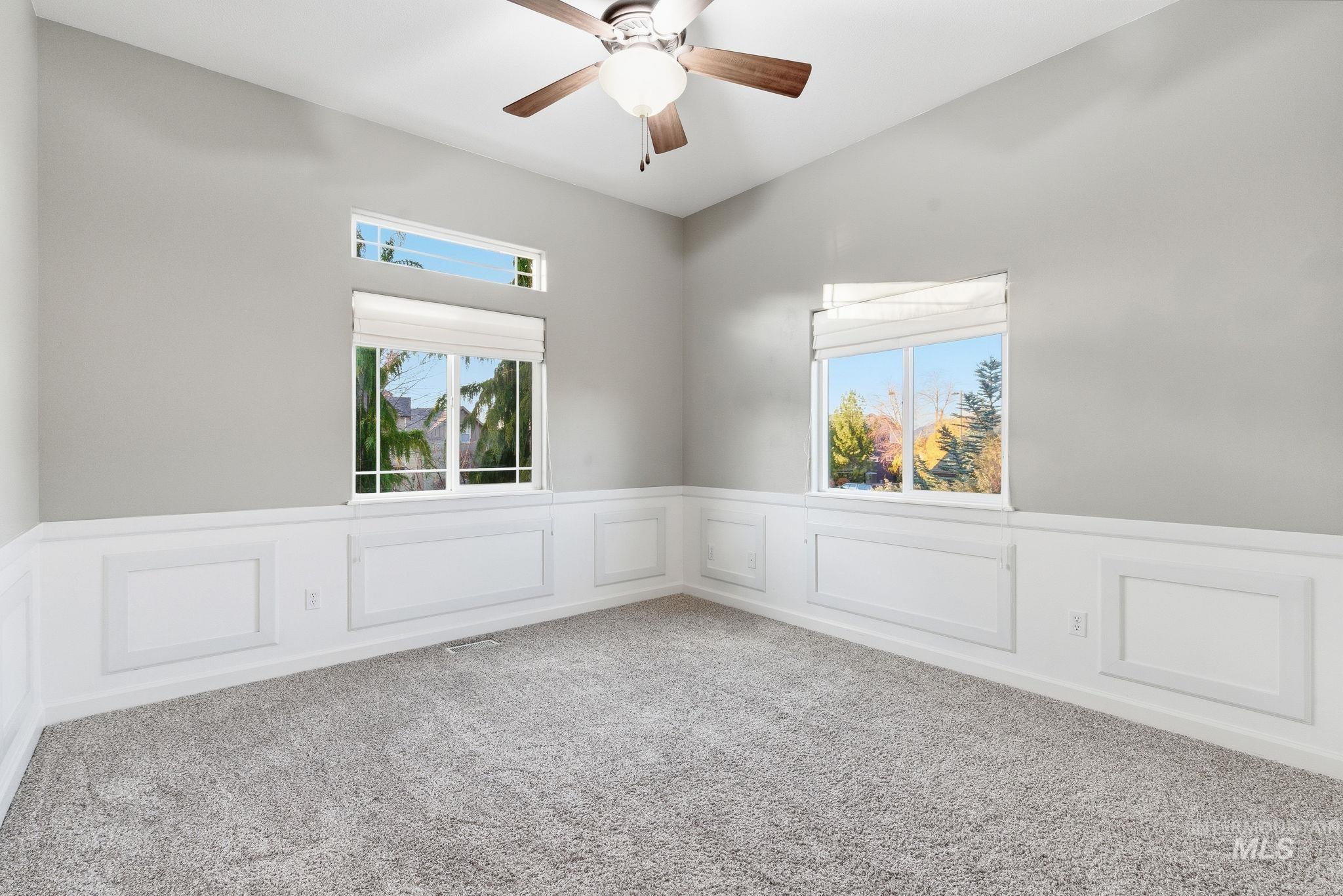 Carpeted spare room with a decorative wall, wainscoting, plenty of natural light, and ceiling fan