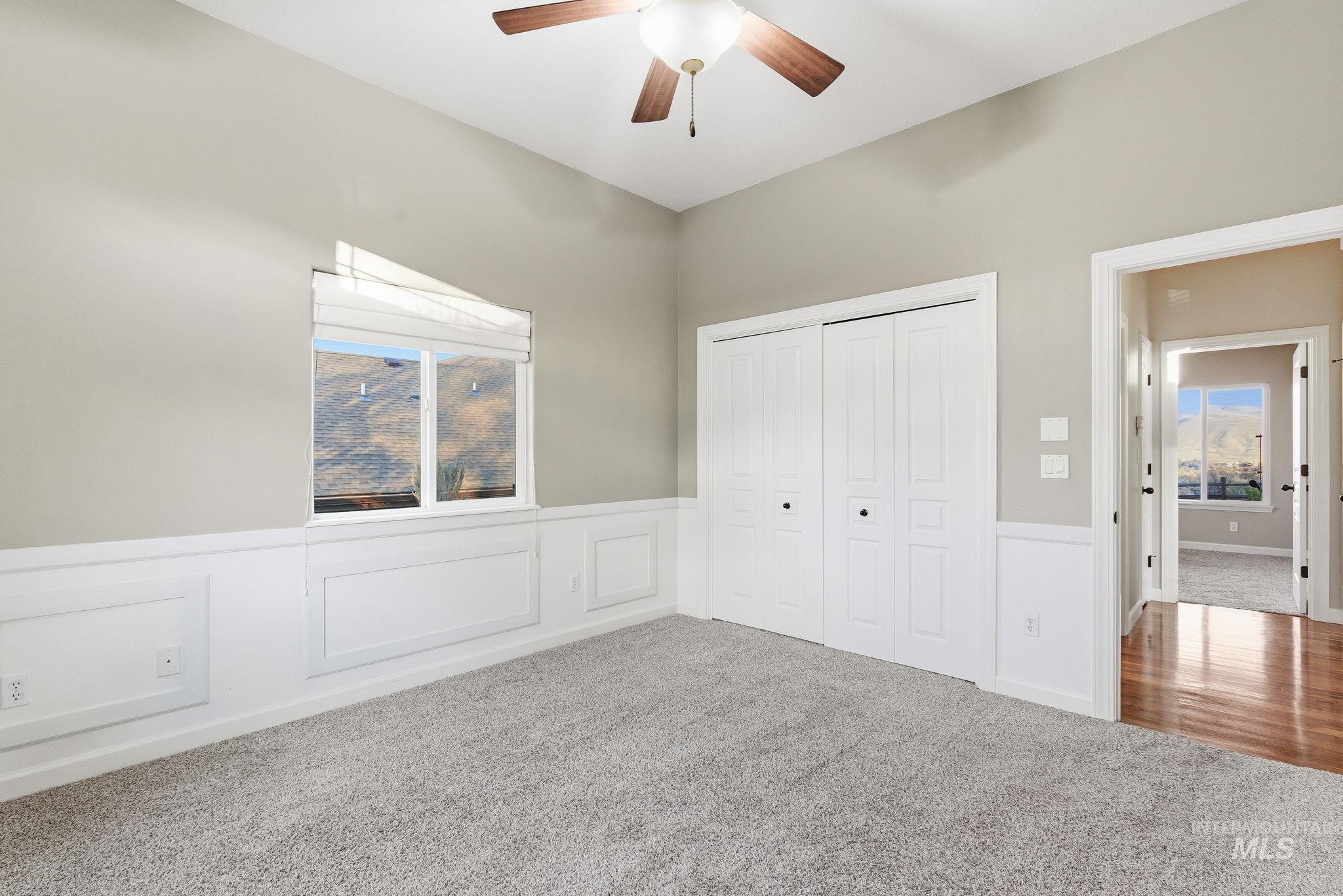 Unfurnished bedroom featuring carpet flooring, a closet, a ceiling fan, and wainscoting