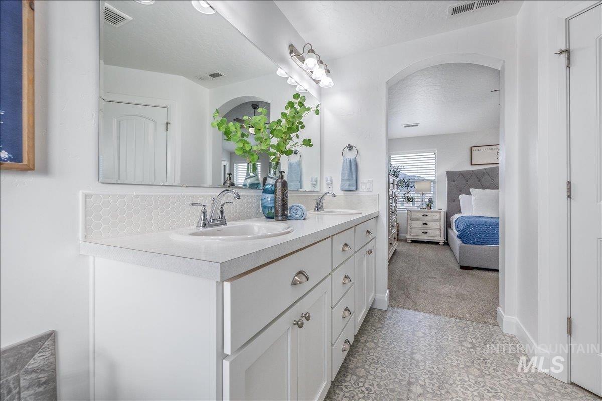 Ensuite bathroom with double vanity, a textured ceiling, and light carpet