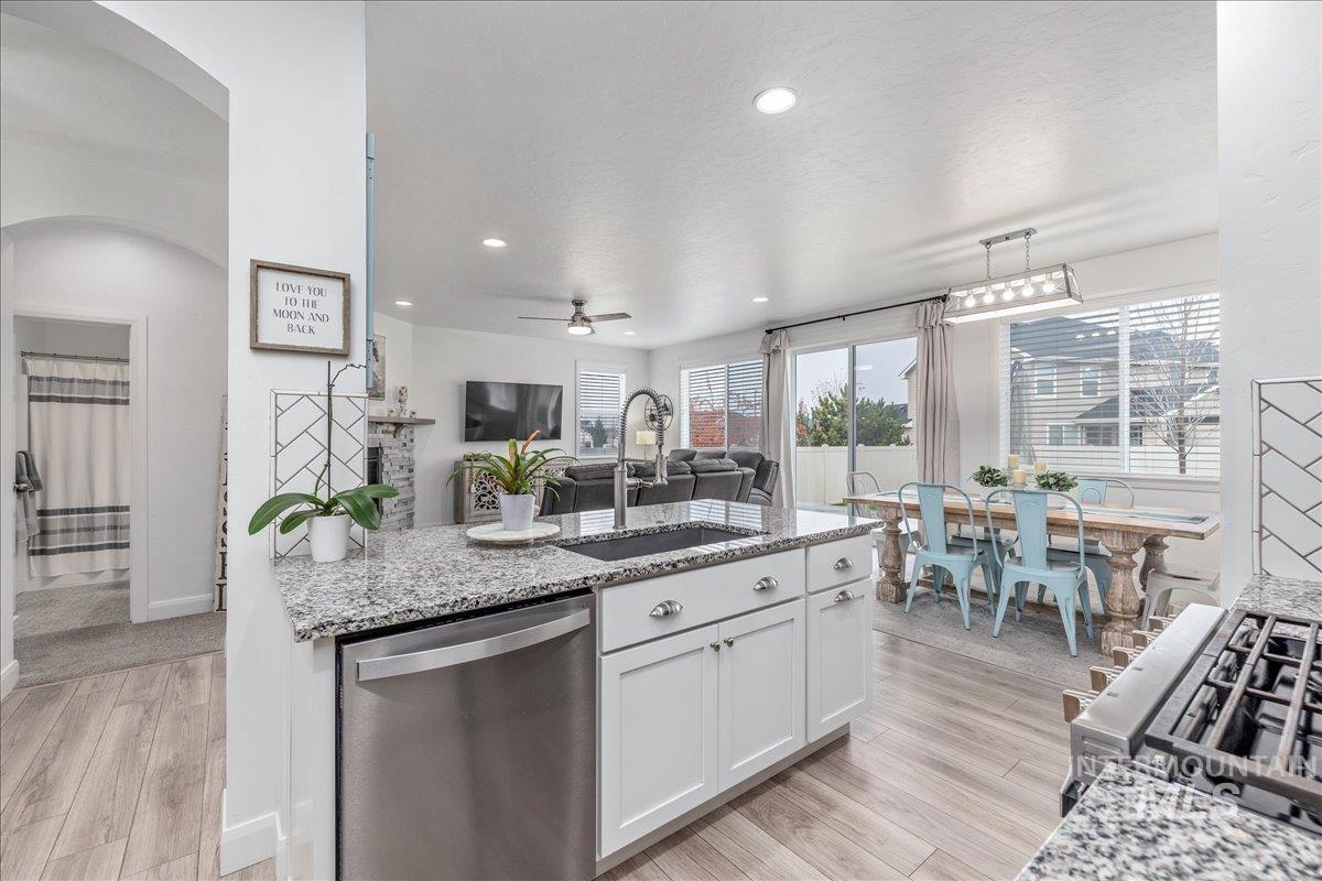 Kitchen featuring appliances with stainless steel finishes, light stone countertops, white cabinetry, light wood-style flooring, and recessed lighting