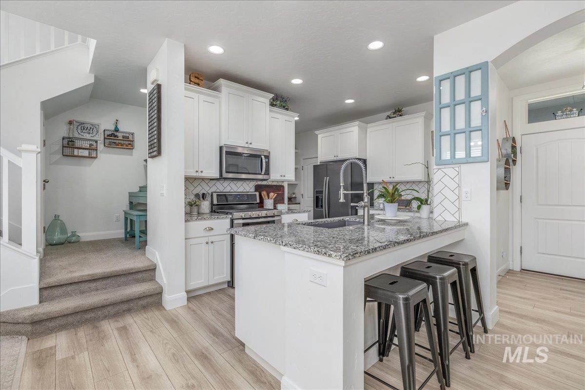 Kitchen featuring a kitchen bar, white cabinets, light stone countertops, backsplash, and recessed lighting