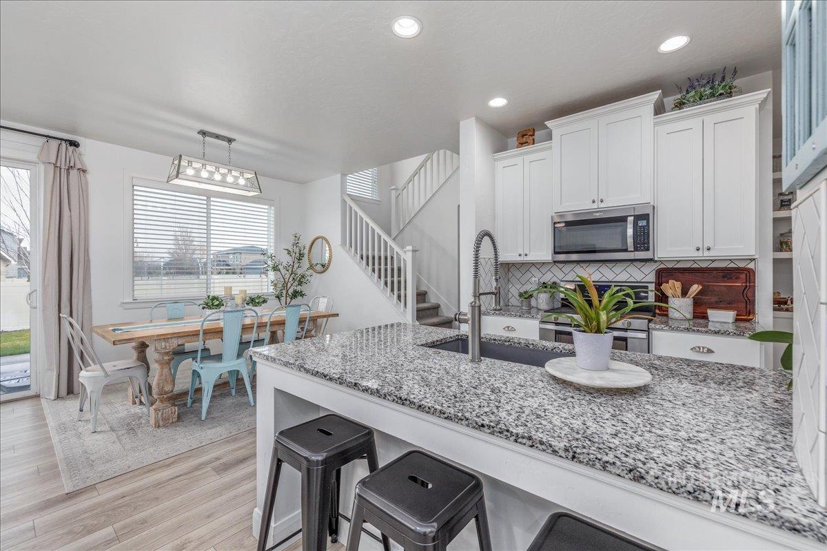 Kitchen with light stone countertops, a kitchen bar, white cabinets, tasteful backsplash, and stainless steel appliances