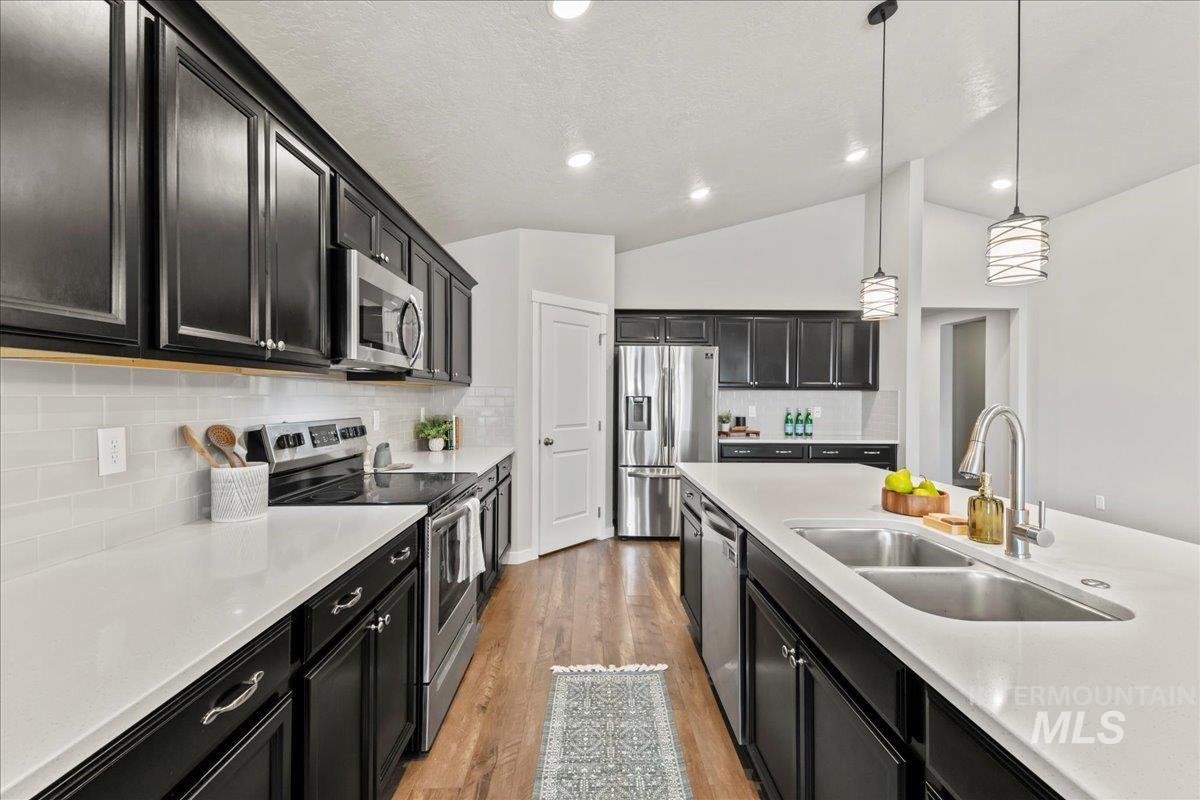 Kitchen with dark cabinetry, appliances with stainless steel finishes, decorative light fixtures, backsplash, and light wood finished floors