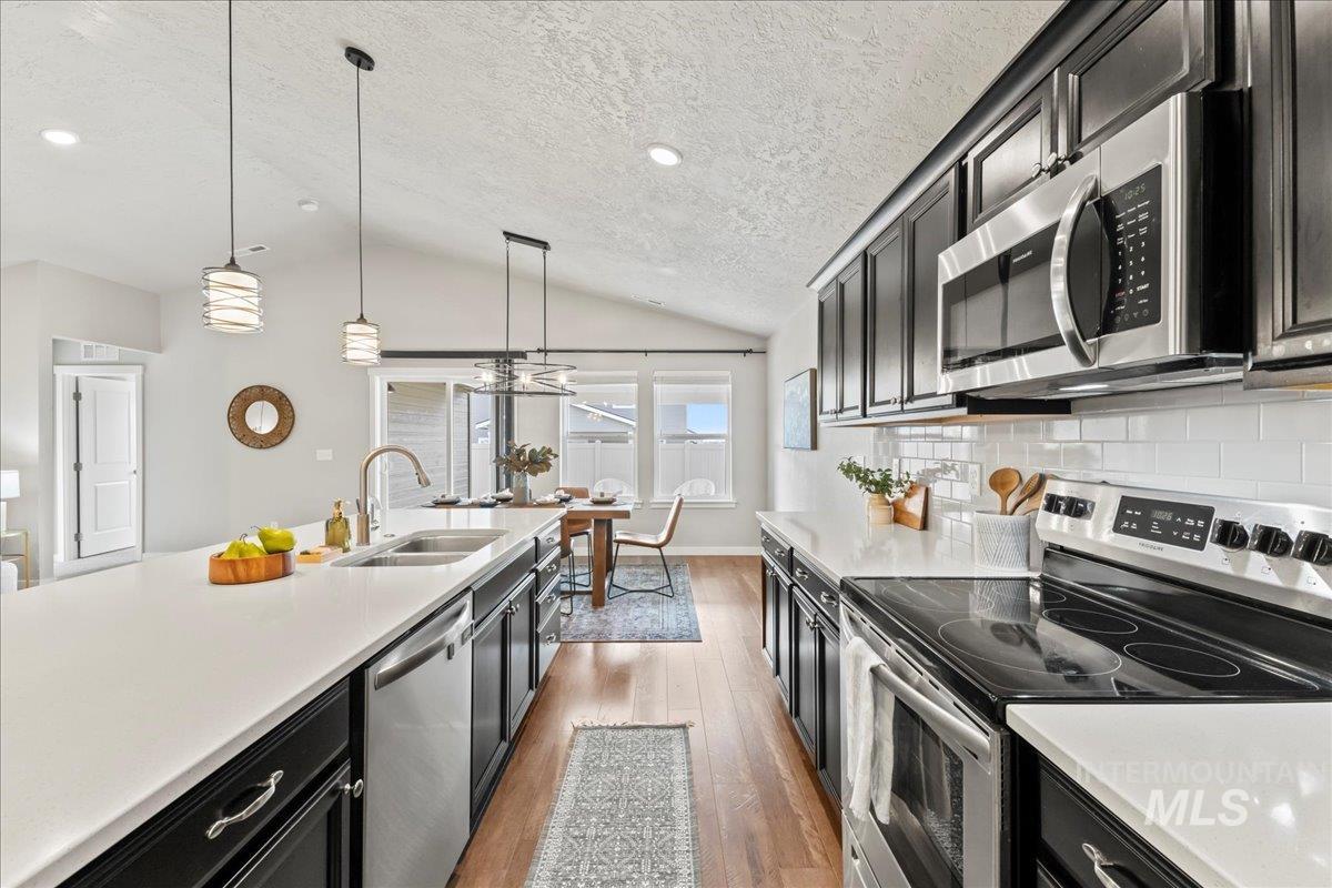 Kitchen with dark cabinetry, stainless steel appliances, dark wood-style floors, a textured ceiling, and hanging light fixtures