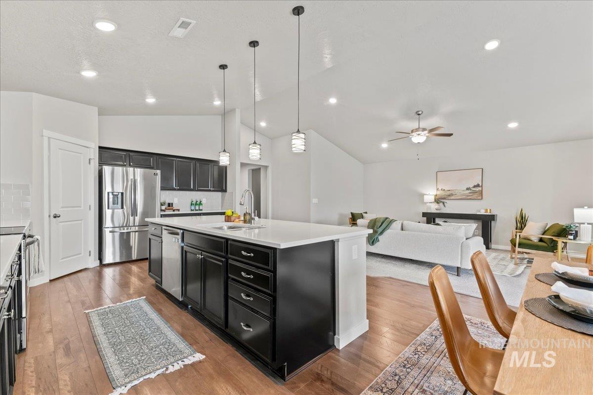 Kitchen featuring decorative backsplash, pendant lighting, vaulted ceiling, a kitchen island with sink, and a ceiling fan