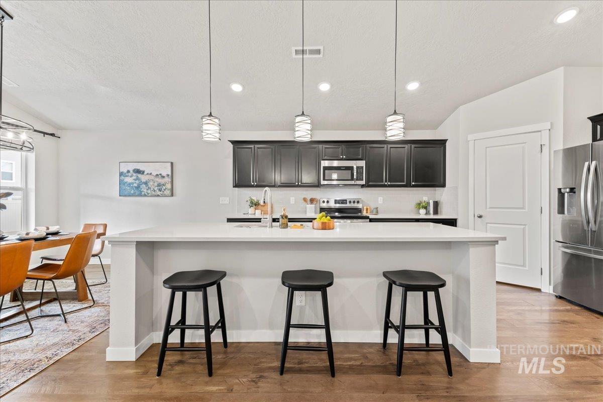 Kitchen with tasteful backsplash, stainless steel appliances, hanging light fixtures, recessed lighting, and a breakfast bar area