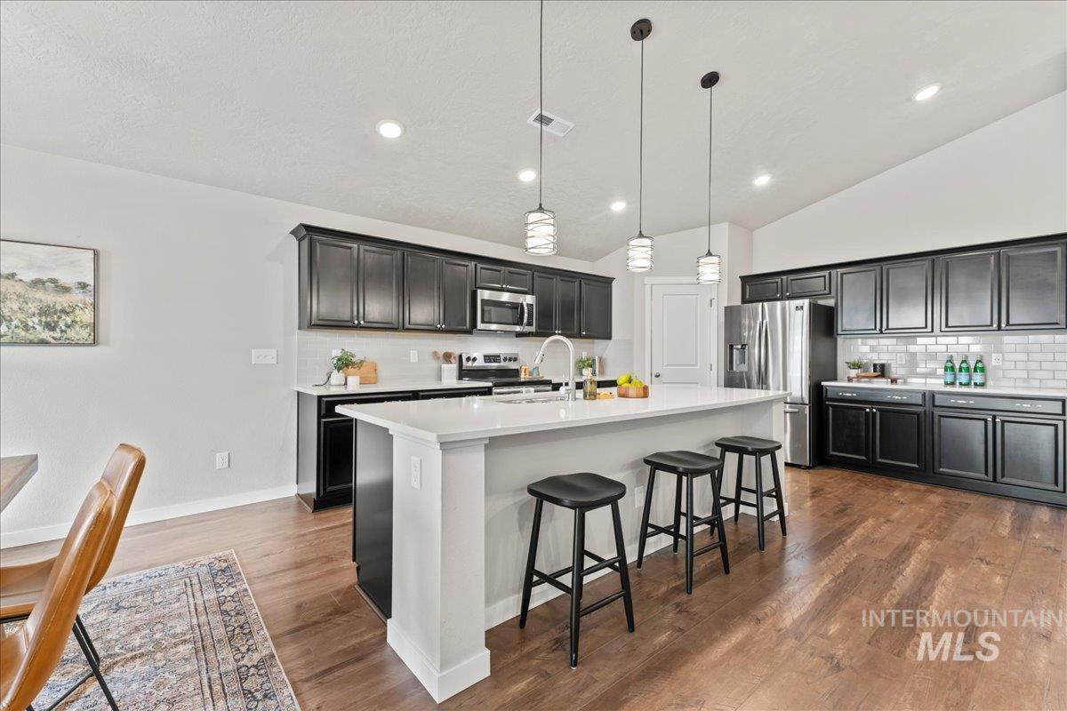 Kitchen featuring backsplash, dark cabinetry, appliances with stainless steel finishes, vaulted ceiling, and recessed lighting