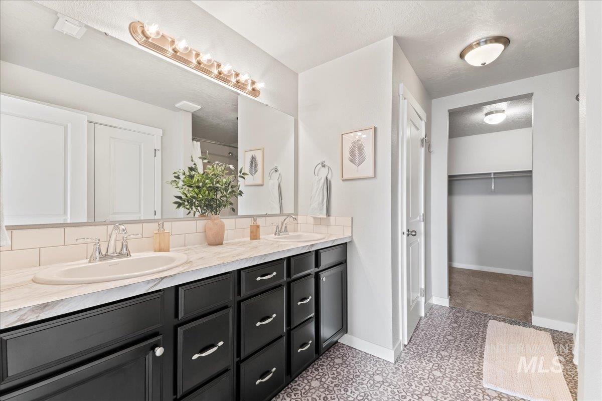 Full bath featuring a textured ceiling, double vanity, and a spacious closet