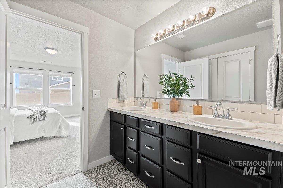 Bathroom with double vanity, a textured ceiling, decorative backsplash, and connected bathroom