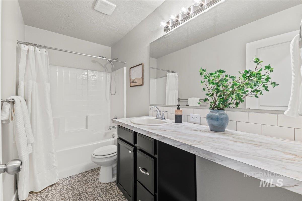 Bathroom with a textured ceiling, shower / bath combination with curtain, and vanity