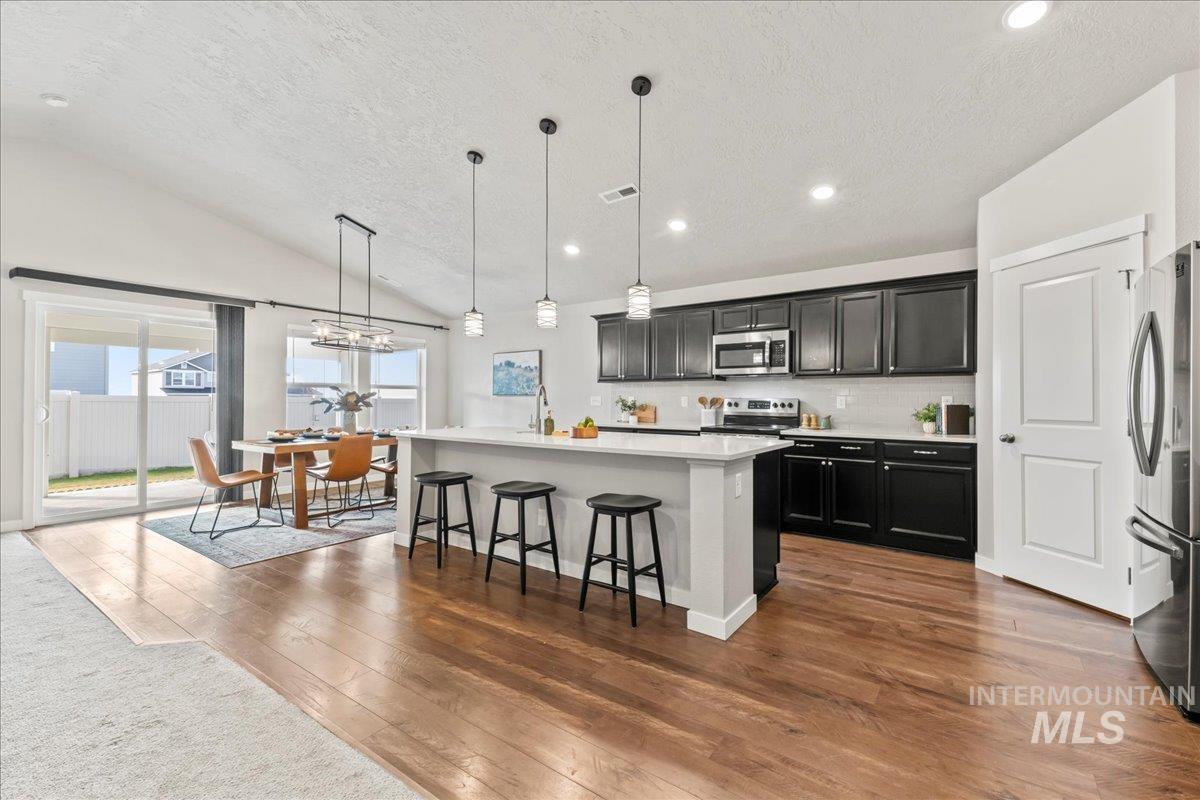 Kitchen featuring dark cabinets, decorative backsplash, hanging light fixtures, a breakfast bar area, and appliances with stainless steel finishes