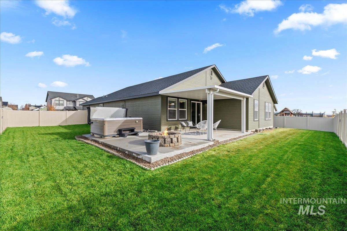 Back of property featuring a fenced backyard, a fire pit, a hot tub, and a patio