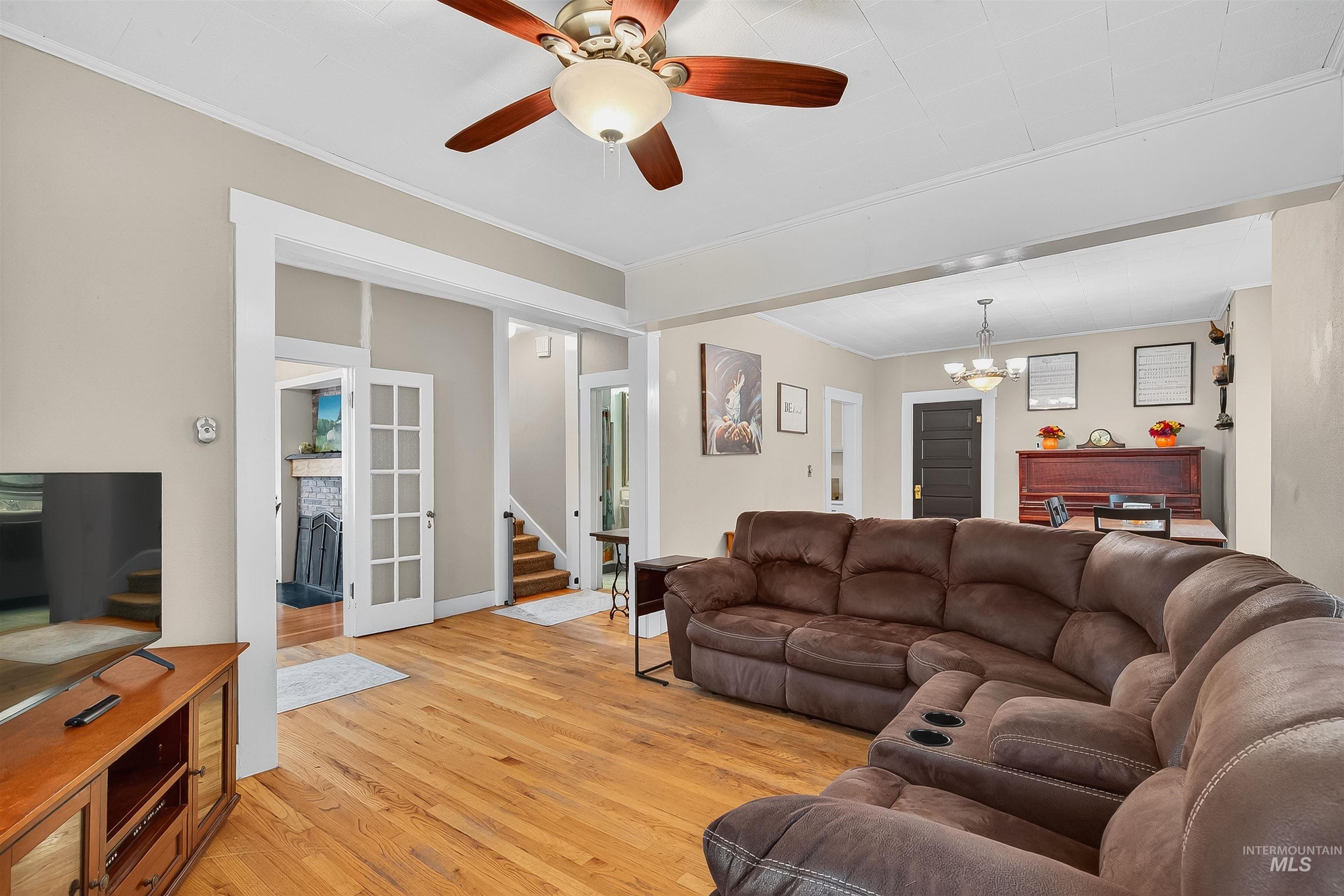 Living room with stairway, light wood-style floors, a ceiling fan, crown molding, and a chandelier