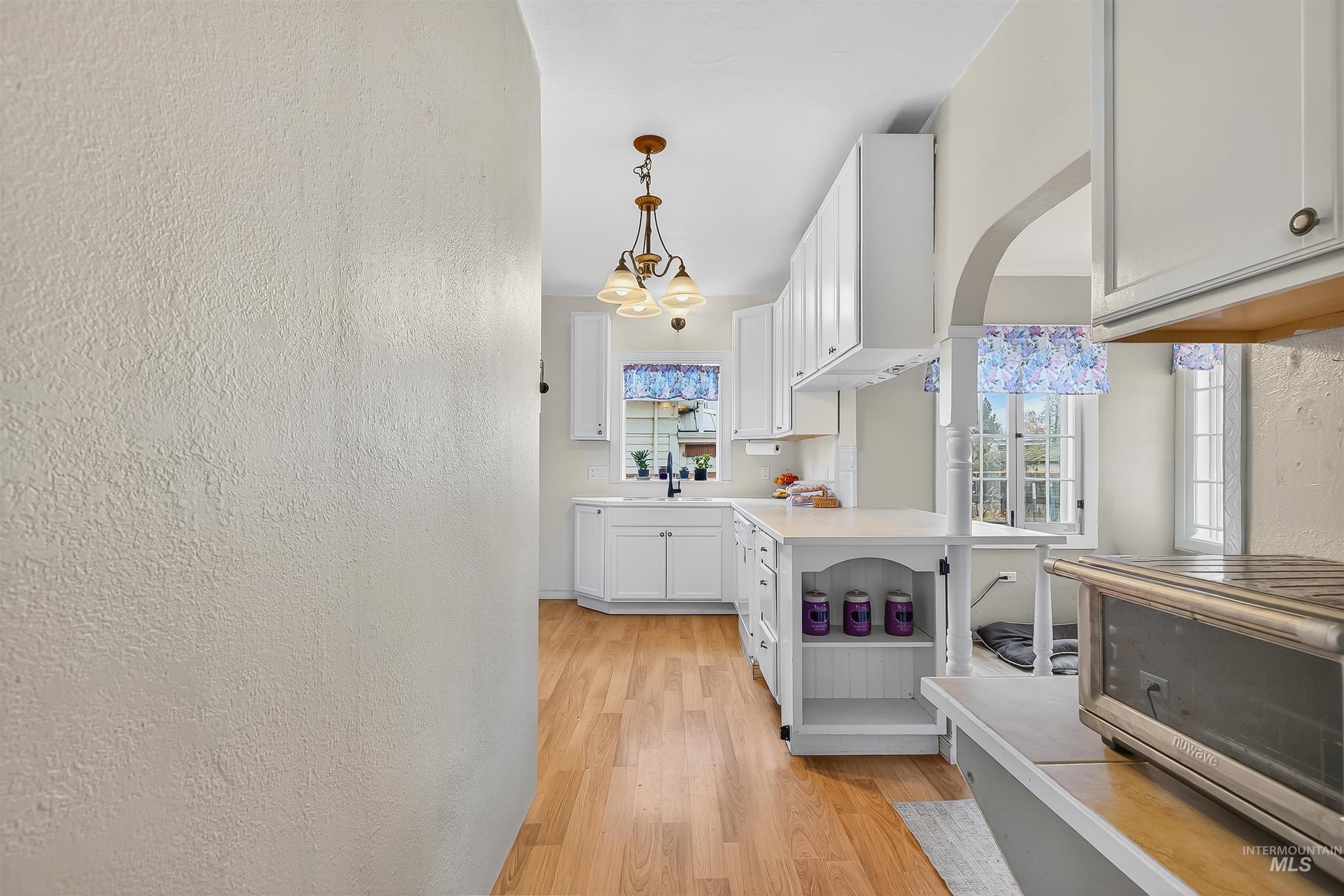 Kitchen featuring a textured wall, light countertops, light wood-style flooring, a chandelier, and white cabinets