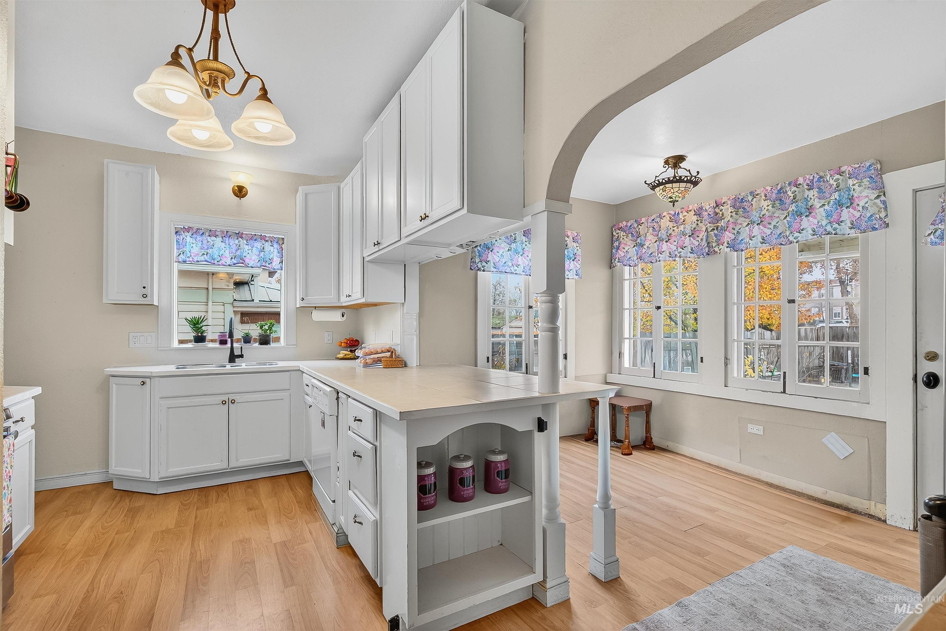 Kitchen with open shelves, a peninsula, white cabinets, light countertops, and a chandelier
