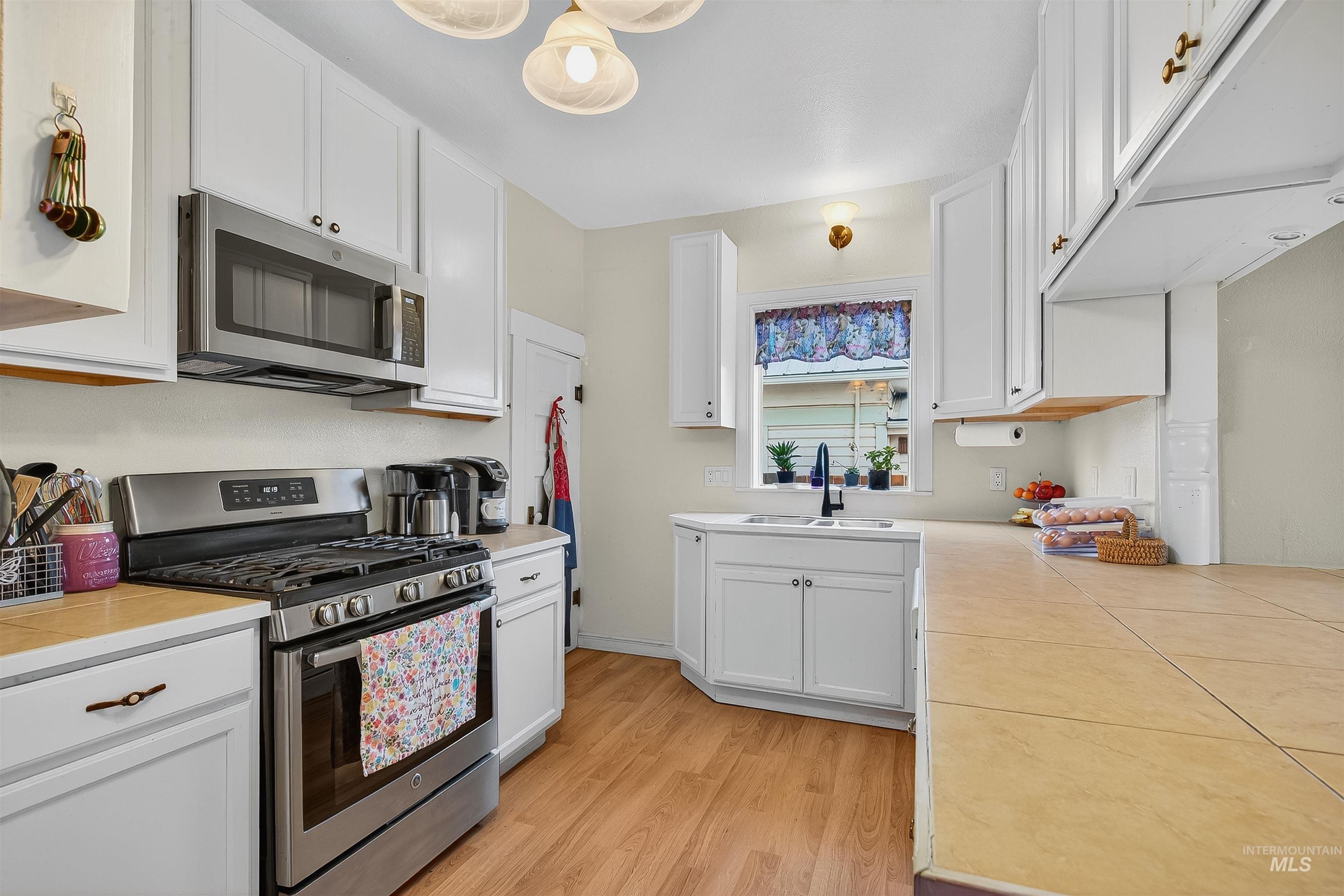 Kitchen with stainless steel appliances, tile countertops, white cabinets, and light wood-type flooring