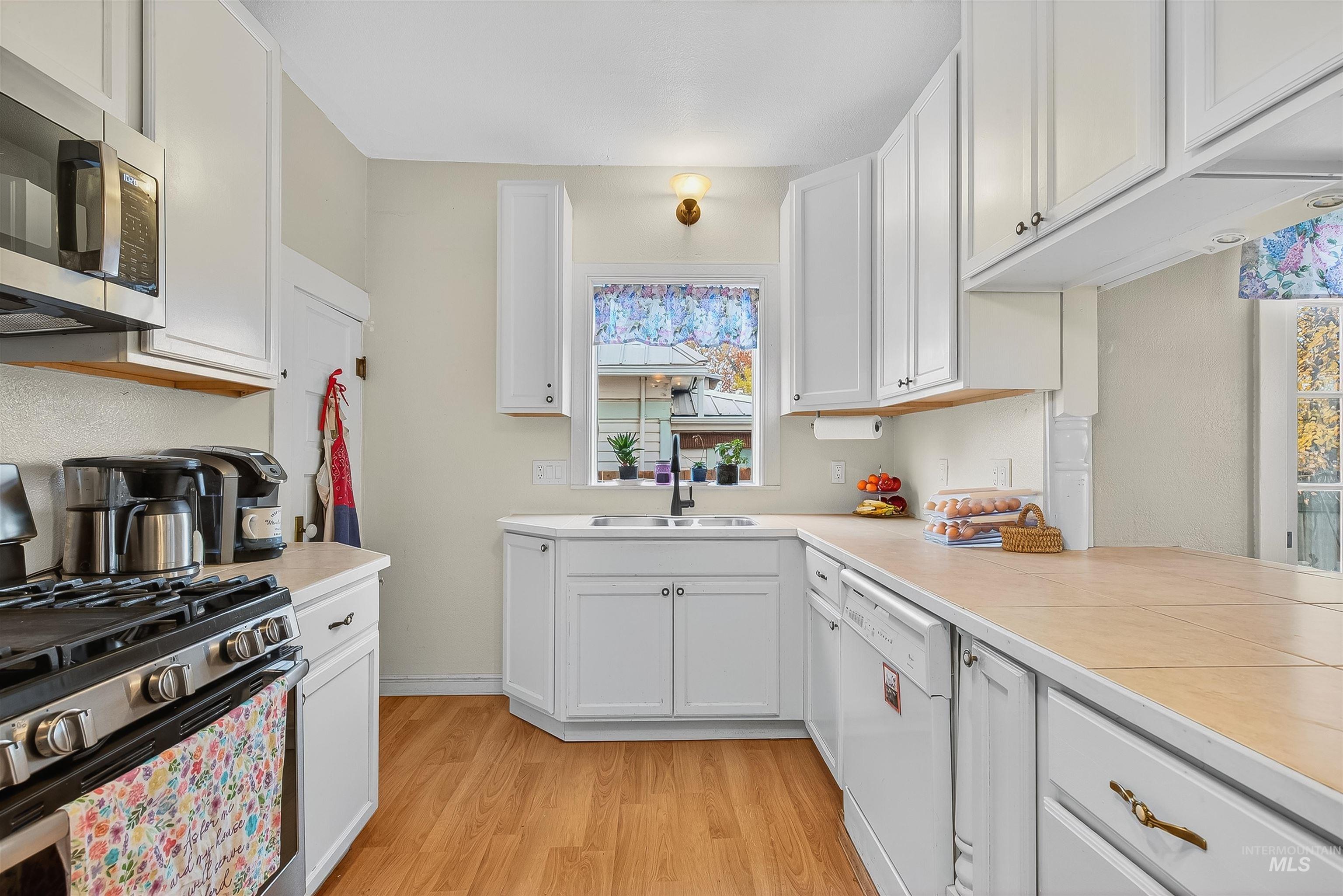 Kitchen featuring appliances with stainless steel finishes, tile counters, white cabinetry, and light wood-style flooring