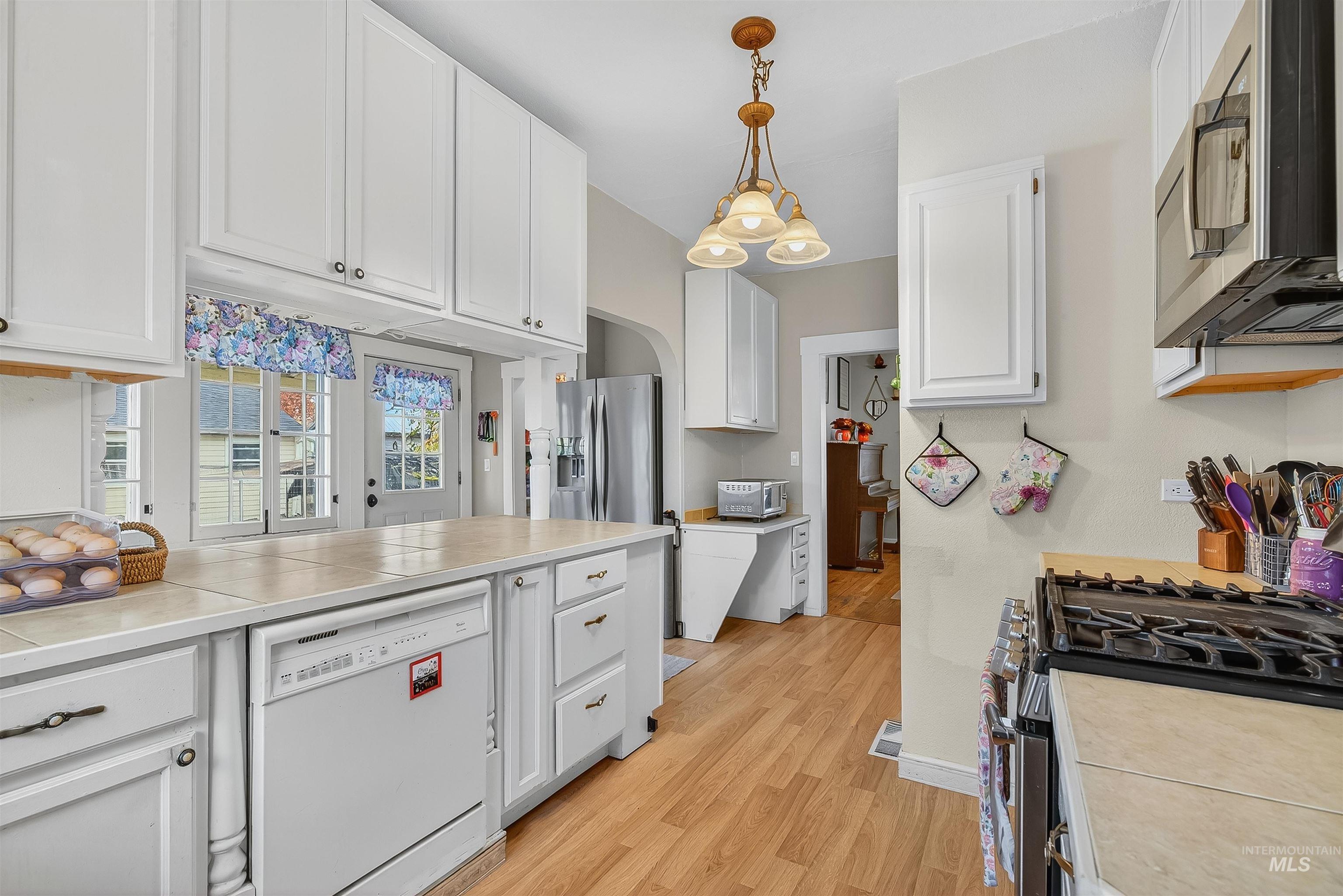 Kitchen featuring tile countertops, appliances with stainless steel finishes, white cabinets, pendant lighting, and light wood-type flooring